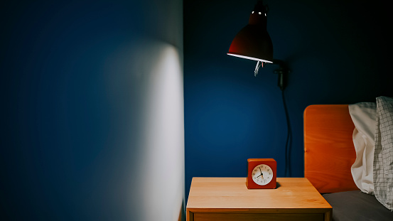 dormitorio por la noche iluminado por lámpara eléctrica con reloj en la mesa de noche al lado de la cama con pared azul photo