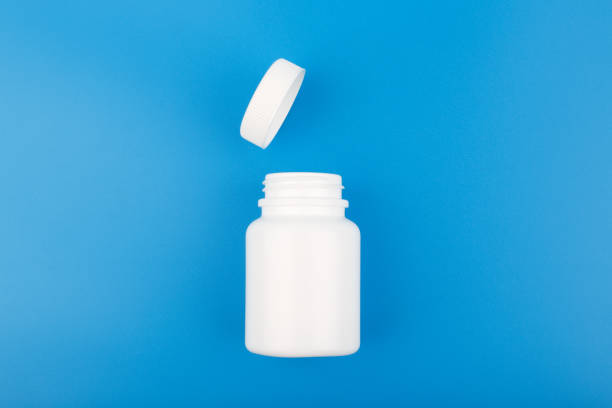 top view of white opened medication bottle against blue background - pill bottle fotos imagens e fotografias de stock