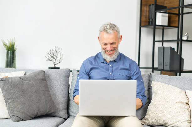 istock Modern middle-aged bearded man using laptop computer sitting on the couch at home 1321504917