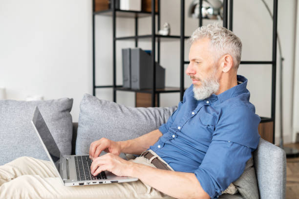 istock Middle-aged bearded man lying down on the couch with a laptop 1321505172