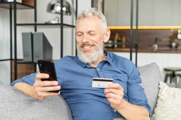 istock Happy optimistic mature man holding smartphone and credit card 1321505370