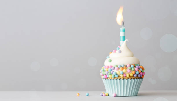 Birthday cupcake with pastel colored sprinkles and a candle Birthday cupcake with pastel colored sprinkles and one birthday cake candle on a gray background with copyspace to side cupcake stock pictures, royalty-free photos & images