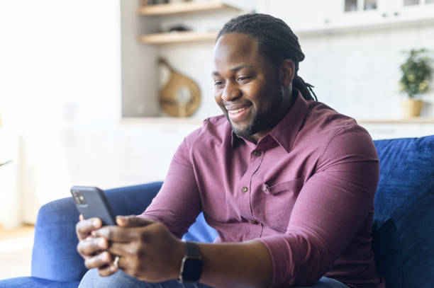 istock Smiling African-American man using smartphone sitting on the sofa at home 1321508616