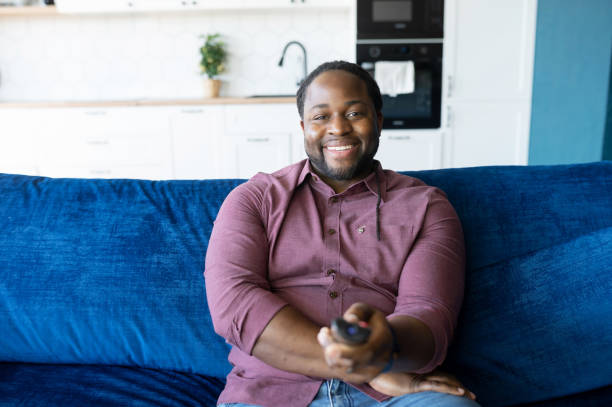istock Cheerful and happy African-American man with dreadlocks holding TV remote controller 1321509912