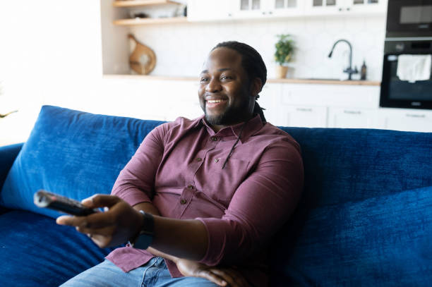 istock Cheerful and happy African-American man with dreadlocks holding TV remote controller 1321509932