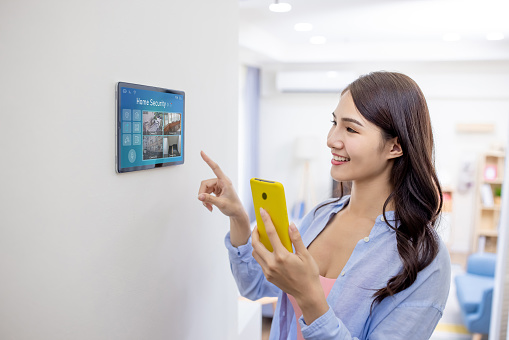close up of asian woman using smart phone connect the digita tablet of home security camera system on wall