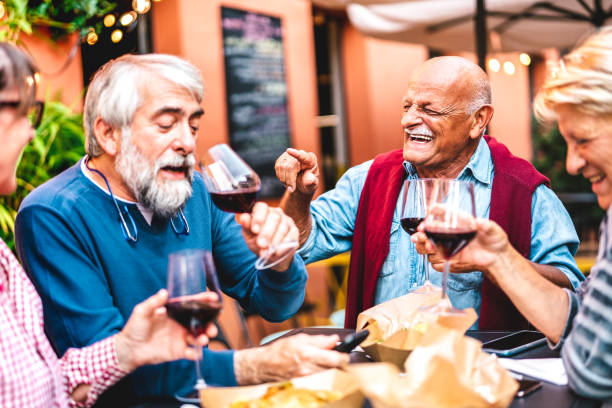 happy retired friends having fun drinking red wine at pre dinner party - senior people eating at restaurant together - dinning life style concept on warm contrast filter - dining senior adult friendship mature adult imagens e fotografias de stock