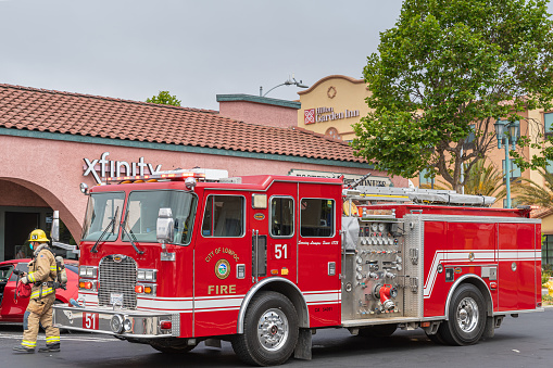 Lompoc, CA, USA - May 26, 2021: Closeup of red fire engine in town with officer and in front of Hilton Garden Inn downtown.