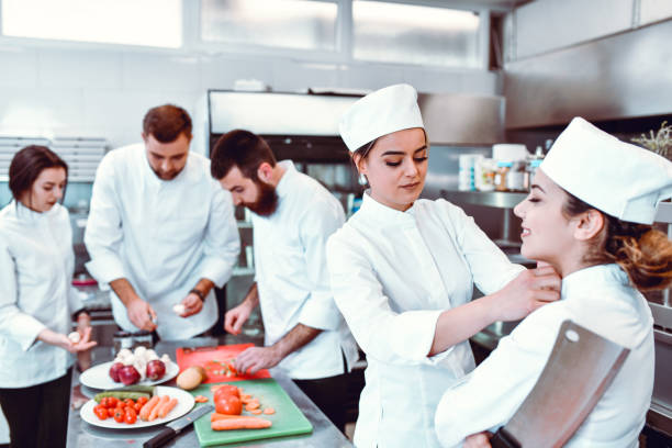 istock Female Chef Fastening Apprentice's Robe While Working On Special Meal With Colleagues 1321531406