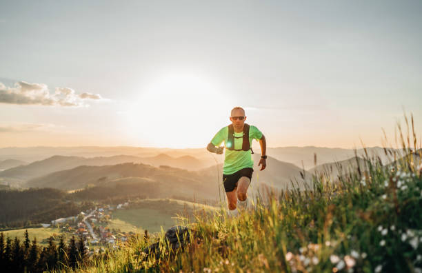istock Active mountain trail runner dressed bright t-shirt with backpack in sport sunglasses running endurance marathon race by picturesque hills at sunset time. Sporty active people concept image. 1321533478