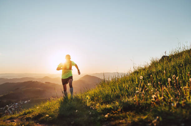 istock Active mountain trail runner dressed bright t-shirt with backpack in sport sunglasses running endurance marathon race by picturesque hills at sunset time. Sporty active people backlight concept image. 1321533479