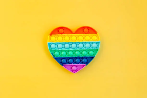 Photo of Top view of colorful markers and anti stress sensory toy pop it rainbow heart on yellow background close up. Creative and funny concepts of children toys. Popular toy. Trend toy 2021 year