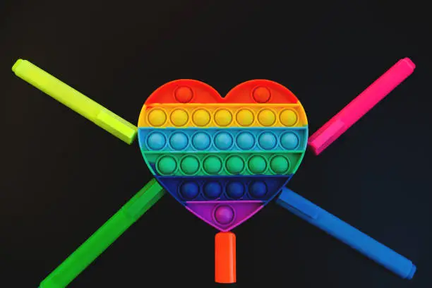 Photo of Top view of colorful anti stress sensory toy pop it rainbow heart on black background close up. Creative and funny concepts of children toys. Popular toy. Trend toy 2021 year.