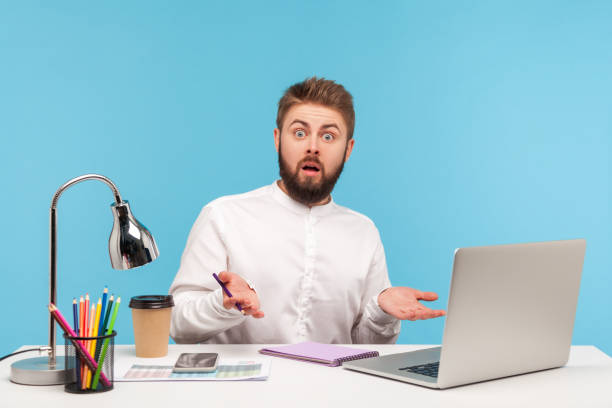 istock Shocked annoyed man office worker spreading hands looking at camera with astonishment, sitting at workplace with laptop and coffee, stressful job 1321536753