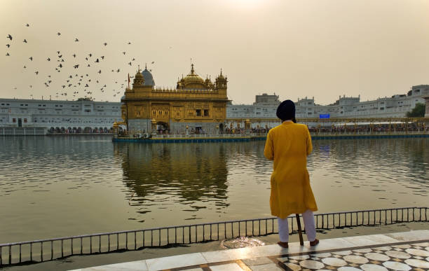 Selective focus of an unidentified male security guard facing towards the Sikh famous Golden temple, wearing the Dastar or turban and holding a spear as protector Amritsar, India - November 06, 2016: Selective focus of an unidentified male security guard facing towards the Sikh famous Golden temple, wearing the Dastar or turban and holding a spear as protector reflectivity stock pictures, royalty-free photos & images