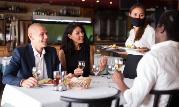 istock Young waitress in protective mask serving guests in restaurant 1321541537