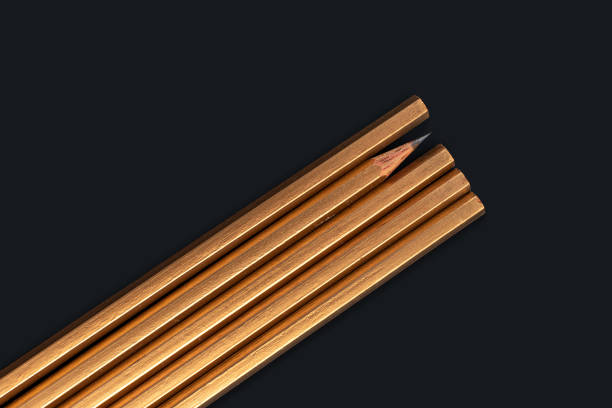 Color image depicting a close up macro view of a collection of colored pencils in a row, on a black background. Selective focus image with one of the pencils in sharp focus with the others blurred out of focus.