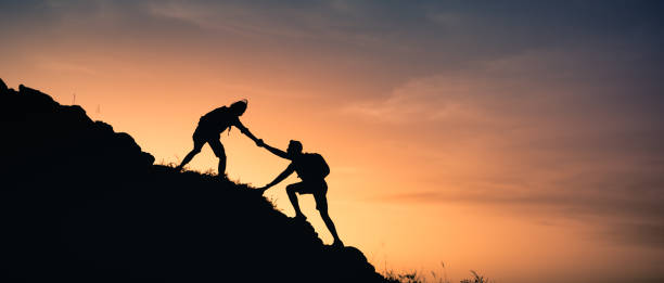istock Two people helping each other climb up a mountain. 1321546699