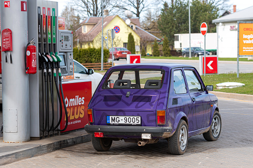 Gulbene, Latvia - May 02, 2021: a colorful vintage car Fiat 126 refueling at the gas station
