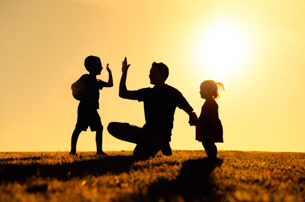 Father playing with his son and little daughter in the park at sunset.