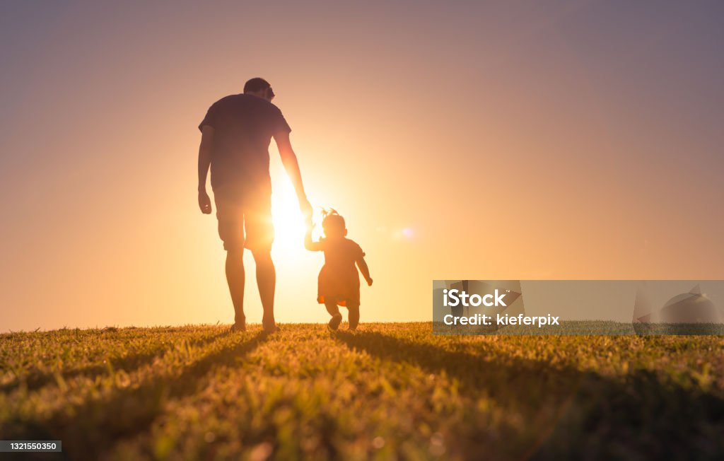 Father and daughter holding hands and walking at sunset outdoors. Father and daughter walking at sunset outdoors. Child Stock Photo