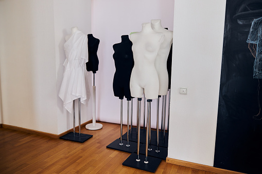 Set of female dummies stands in white wall aumbry near blackboard in light fashion design studio. Equipment for tailors and clothes designers work