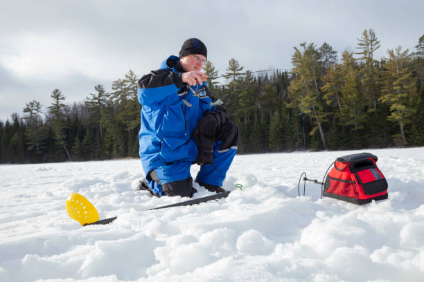 homme pêche sur glace sur un lac du nord du minnesota par un matin d’hiver ensoleillé - ice fishing photos et images de collection