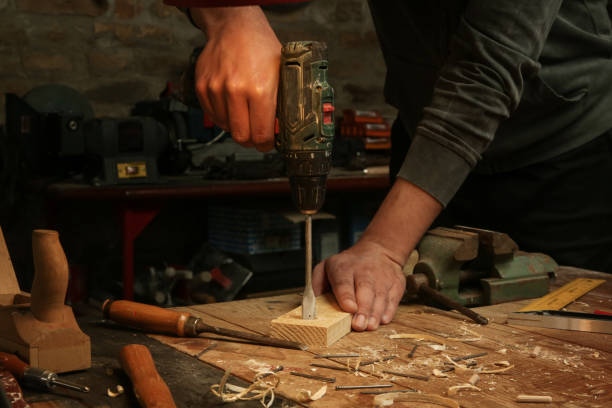 istock Carpenter hammering nail into wooden plank in workshop. 1321561100