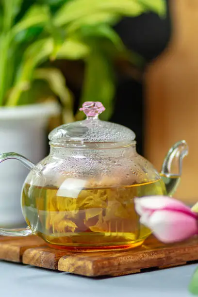 green tea with rose petals in a transparent teapot on a wooden table on a black background. The background is blurred. Tea drinking