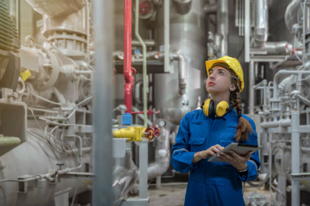 Female engineer smiling with yellow hard hat helmet and holding tablet working in factory stock photo