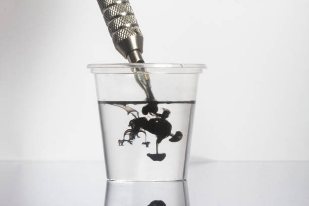 istock Tattoo machine cleaning black ink needles with clean water in clear glass 1321574478