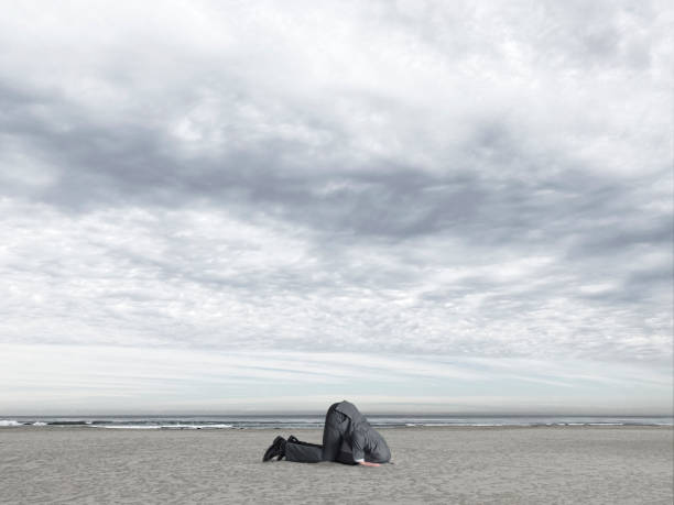 Man With Head Buried In The Sand A businessman's head is buried in the sand as he crouches down at the seashore. head in the sand stock pictures, royalty-free photos & images
