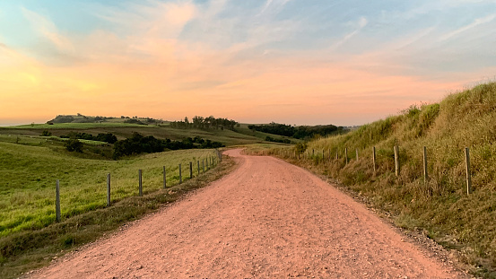 Gravel road at dawn, through green pastures towards mountains, in the countryside