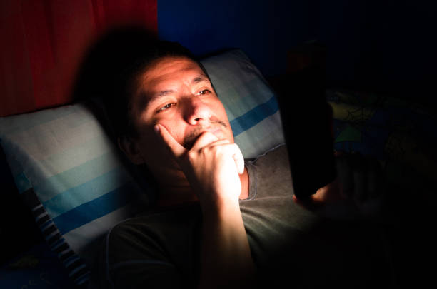 istock Sleepless and thinking man using his mobile phone in bed in the dark. 1321590948