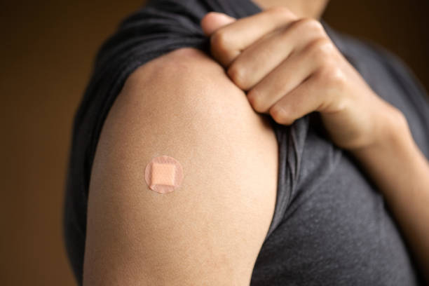 Young Person showing vaccinated shoulder with round adhesive bandage Young person showing vaccinated shoulder with round adhesive bandage rolled up sleeves stock pictures, royalty-free photos & images