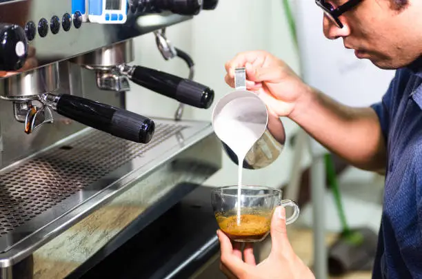 Photo of Hand of barista making latte or cappuccino coffee, pouring milk making latte art.