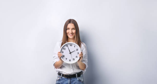 istock Beautiful young woman holding a clock on grey background 1321598087