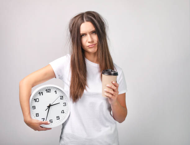 Beautiful young woman with clock and coffee on grey background