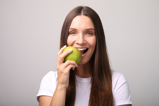 Beautiful young woman with apple on grey background