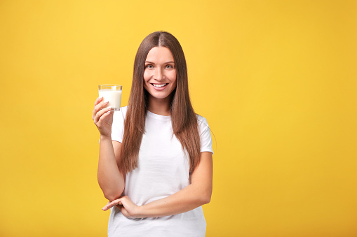 Beautiful young woman with milk on yellow background