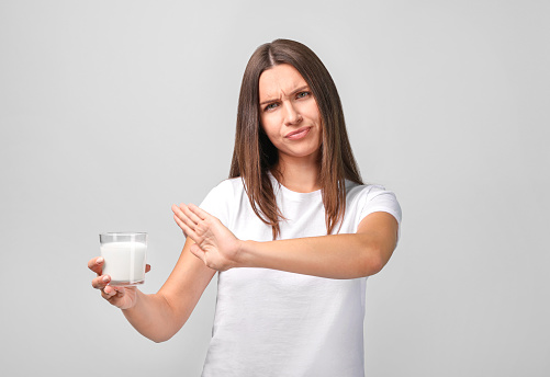 Young woman with milk on grey background. Lactose intolerance, health care concept.