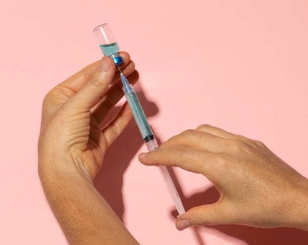 istock Hands filling syringe from vial with hard shadows on pink background 1321599520
