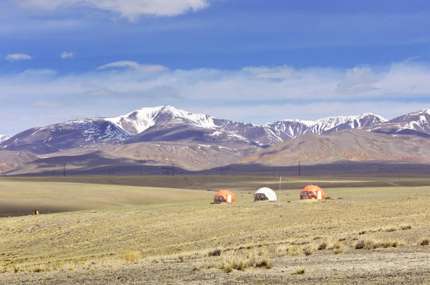 Tourist camping under spherical roofs in the Chui steppe in spring against the background of the snow-covered Kurai ridge under the blue sky. Siberia, Russia