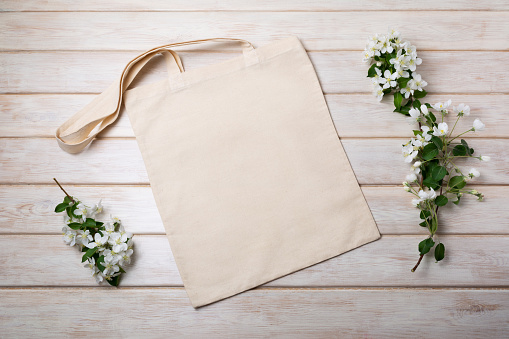Canvas tote bag mockup with blooming apple tree branch on the white wooden table. Rustic linen shopper bag mock up for branding presentation