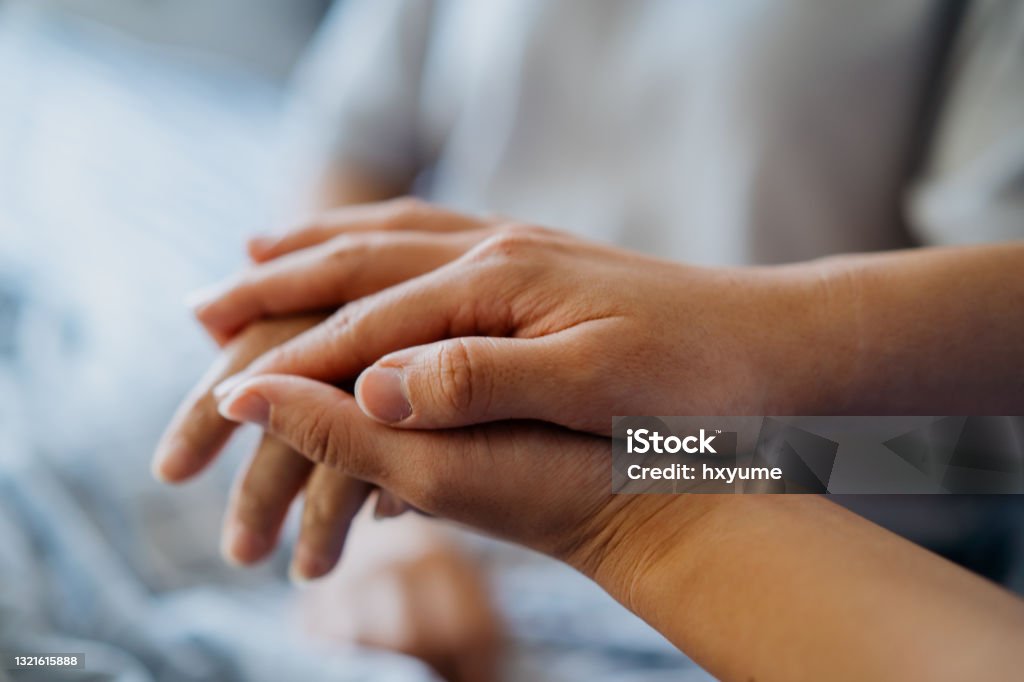 Healthcare worker holding hand of a patient resting on bed Close up shot of hand of a female healthcare worker holding hand of a patient resting on bed, giving her support, encouragement and care. Doctor home healthcare visit. Nurse Stock Photo