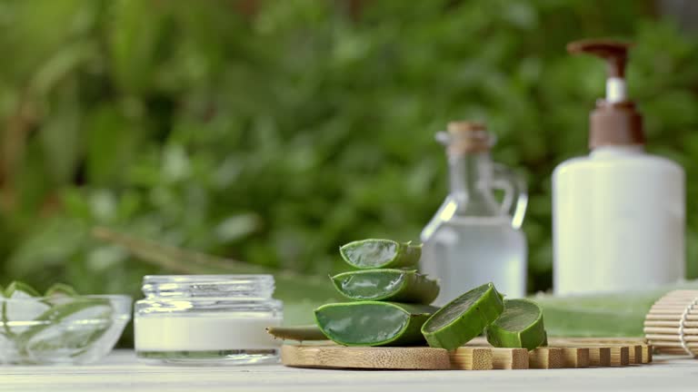 Panning shot of aloe vera slices and moisturizer on a wooden table. Beauty treatment concepts