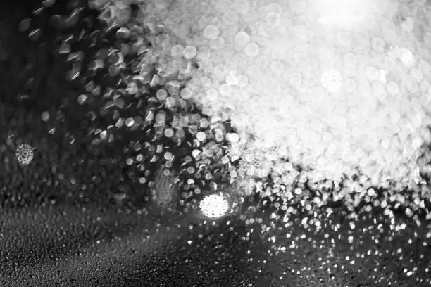 Photo of Water droplets on glass at night, dark background. Black and white texture. Defocus and blur