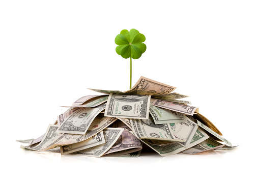 Earning a fortune. Four leaf clover on top of a pile of dollar bills.