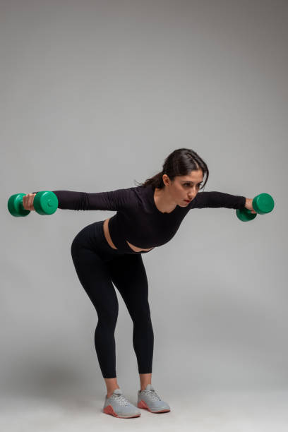 athletic girl doing shoulders exercises with dumbbells on grey background - body building determination deltoid wellbeing imagens e fotografias de stock