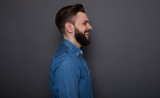 Close up side view photo of handsome bearded modern hipster man in jeans shirt on the gray background